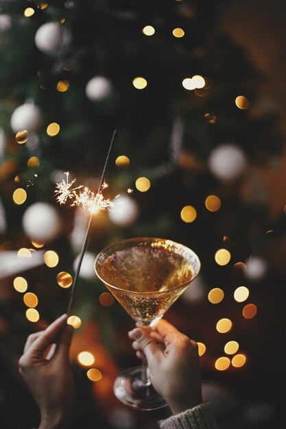 Foto feliz ano novo mulher comemorando com fogos de artifício e taça de champanhe contra as luzes da árvore de natal