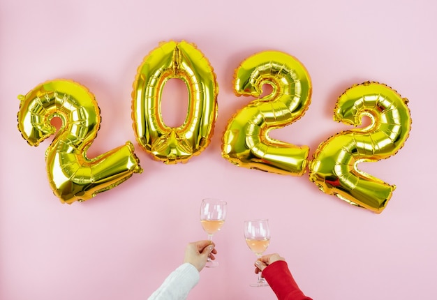 Feliz Ano Novo. Números 2022. Mãos com óculos brindando no fundo rosa. Copie o espaço.