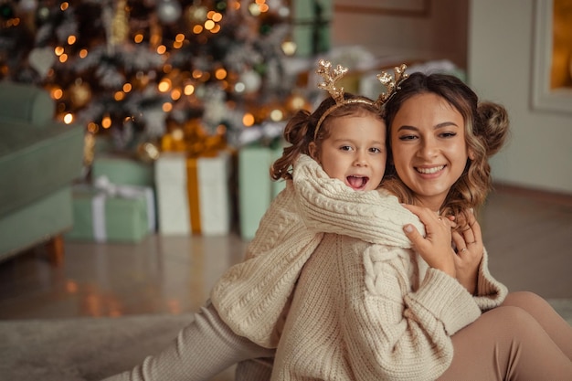Feliz ano novo tradições familiares jovem mãe e sua filha se divertem em casa perto da árvore de natal e da lareira