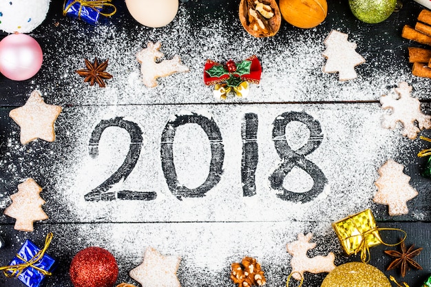 Feliz año nuevo 2018 escrito en harina y decoraciones de Navidad Galletas de jengibre, canela, naranjas, especias, nueces y cortadores de galleta sobre fondo de madera. Tarjeta de Navidad, tarjeta de felicitación de año nuevo