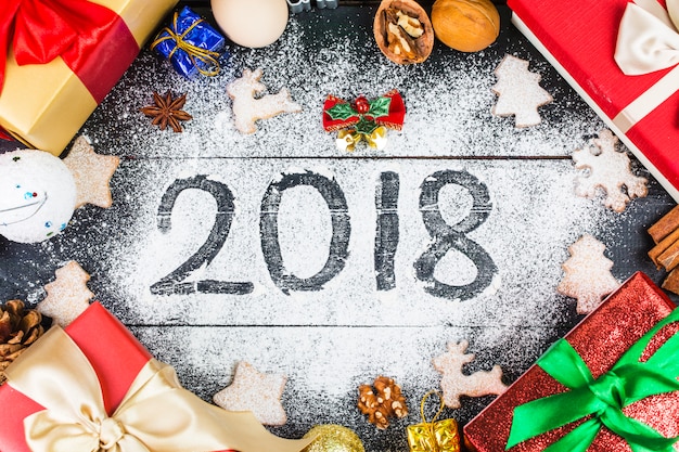 Feliz año nuevo 2018 escrito en harina y decoraciones de Navidad Galletas de jengibre, canela, naranjas, especias, nueces y cortadores de galleta sobre fondo de madera. Tarjeta de Navidad, tarjeta de felicitación de año nuevo