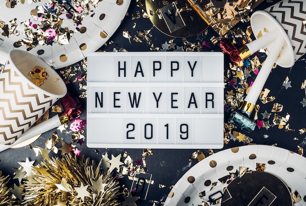 Feliz año nuevo 2019 en la caja de luz con taza para fiestas, soplador de fiestas, malla, confeti