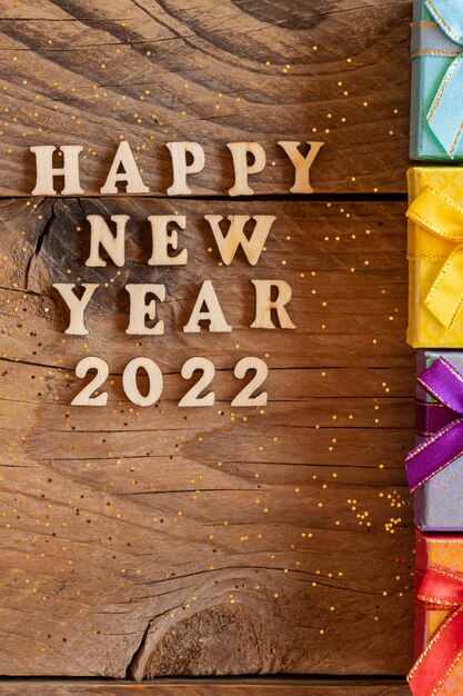 Feliz año nuevo 2022. Cita de letras de madera y números 2022 sobre fondo de madera con pequeñas cajas de regalo multicolores. Concepto creativo para tarjeta de felicitación de año nuevo.