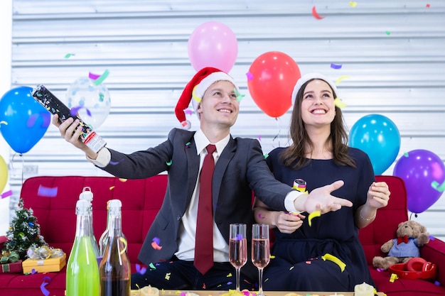 Feliz año nuevo 2022 concepto, pareja feliz encendiendo fuegos artificiales de papel con champán y galletas sobre la mesa en la fiesta de Navidad y año nuevo después de terminar el trabajo comercial.