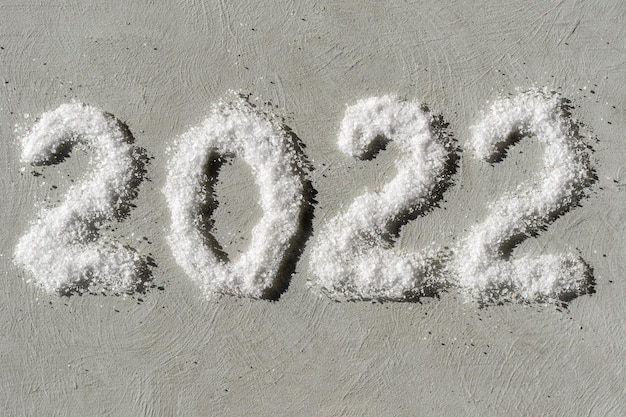 Feliz año nuevo 2022. La fecha 2022 está escrita en sal como nieve sobre un fondo de yeso gris áspero. Objeto de superposición creativa para postales.