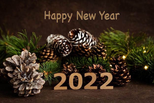 Feliz año nuevo 2022 en el fondo de chocolate de conos ramas de pino y guirnaldas