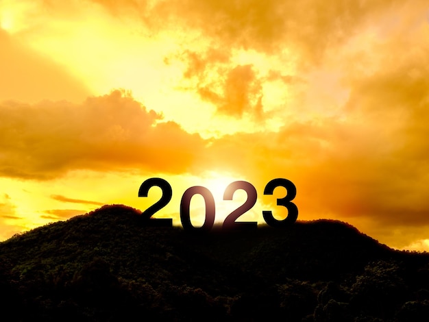 Feliz año nuevo 2023 con grandes letras de silueta en la montaña con hermosa luz de sol luz del sol cielo dorado y nubes para el concepto de éxito Bienvenido Feliz Navidad y feliz año nuevo en 2023