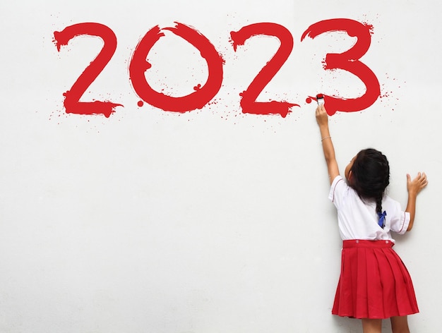 Feliz año nuevo 2023 Niña sosteniendo un pincel pintando sobre un fondo de pared blanca Concepto de idea de regreso a la escuela