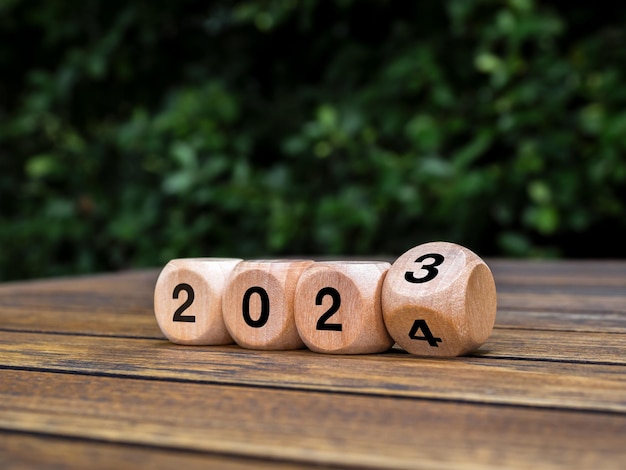 Feliz año nuevo 2024 con el inicio de nuevas tendencias de historias y negocios Conceptos de sostenibilidad ambiental Voltear números de 2023 a 2024 en bloques de cubos de madera ecológica sobre fondo de hojas verdes de mesa de madera