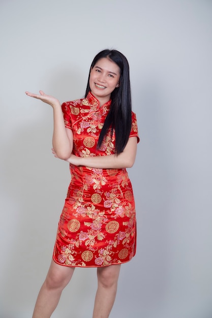 Feliz Año Nuevo Chino. Hermosa mujer asiática con vestido tradicional cheongsam qipao con gesto de felicitación aislado en superficie gris claro con espacio de copia