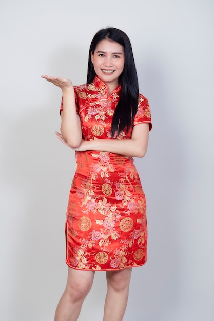 Feliz Año Nuevo Chino. Hermosa mujer asiática con vestido tradicional cheongsam qipao con gesto de felicitación aislado en superficie gris claro con espacio de copia