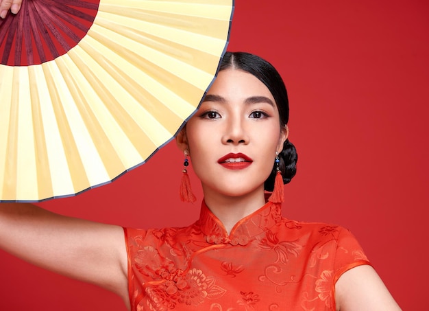 Feliz Año Nuevo Chino. Mujer asiática con vestido tradicional cheongsam qipao sosteniendo un ventilador aislado de fondo rojo.