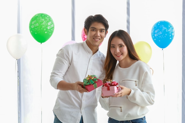 Feliz año nuevo y concepto de pareja. El hombre joven y la mujer asiáticos sonríen y sostienen la caja de regalo linda en partido.