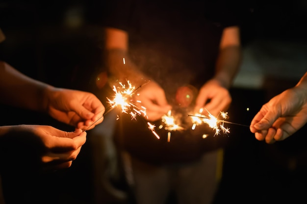 Feliz año nuevo y feliz navidad grupo de personas familia con concepto de iluminación de fuego de bengala Mano sosteniendo una luz de fuegos artificiales de bengala ardiente primer plano mujer mano con brillo oscuro Concepto de año nuevo