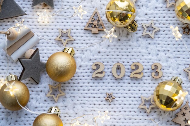 Feliz año nuevo, letras de madera y números 2023 sobre un fondo festivo de punto blanco con lentejuelas, estrellas, luces de guirnaldas, saludos, postal, portada del calendario