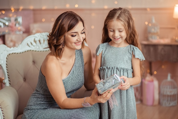 ¡Feliz año nuevo! madre e hija se dan un regalo en el fondo de lei de navidad en casa