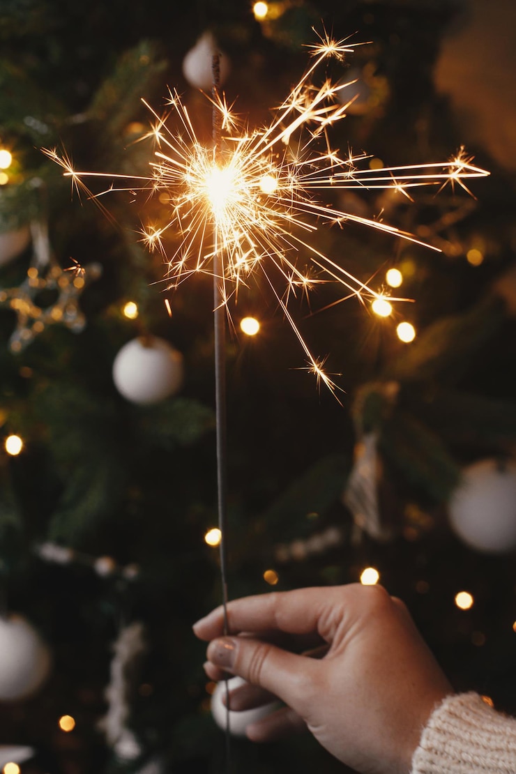 Foto feliz año nuevo mano sosteniendo una bengala ardiente en el fondo de las luces del árbol de navidad en vísperas