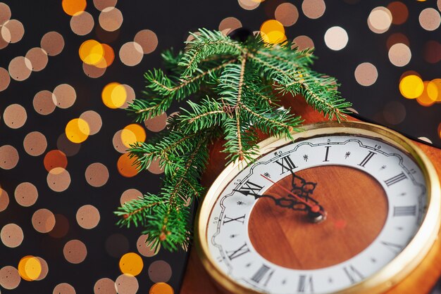 Feliz año nuevo a la medianoche, antiguo reloj de madera con luces navideñas y ramas de abeto