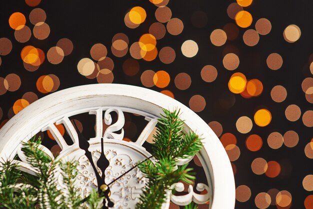 Feliz año nuevo a la medianoche, antiguo reloj de madera con luces navideñas y ramas de abeto