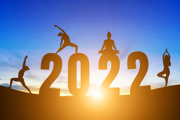 Feliz año nuevo números 2022, silueta mujer practicando yoga amanecer temprano en la mañana sobre el fondo del horizonte, concepto de salud y feliz año nuevo.