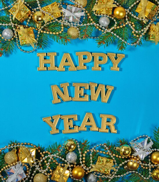 Foto feliz año nuevo texto dorado y rama de abeto y adornos navideños sobre un fondo azul.