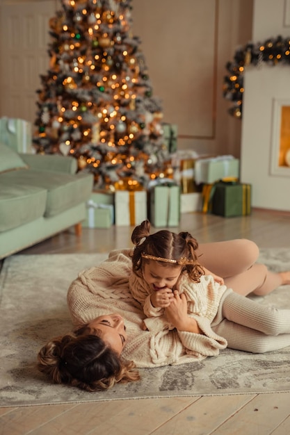 Feliz Año Nuevo tradiciones familiares la joven madre y su hija se divierten en casa cerca del árbol de Navidad y la chimenea