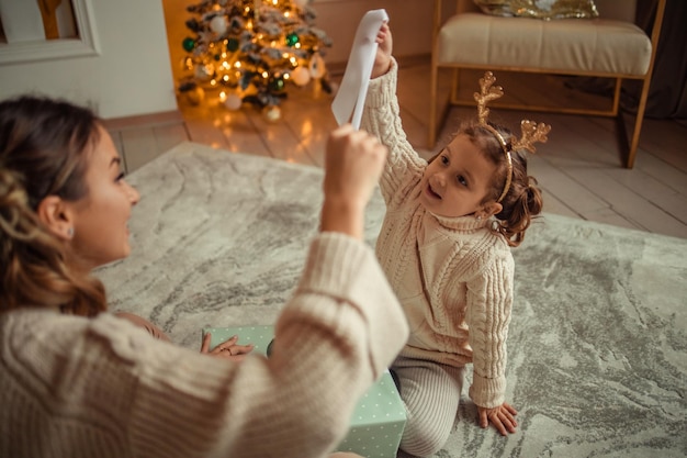 Feliz Año Nuevo tradiciones familiares la joven madre y su hija se divierten en casa cerca del árbol de Navidad y la chimenea