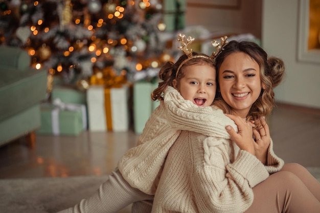 Feliz Año Nuevo tradiciones familiares la joven madre y su hija se divierten en casa cerca del árbol de Navidad y la chimenea