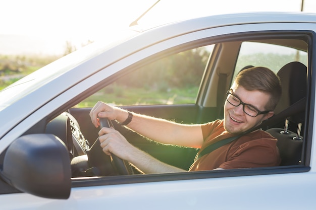 Foto feliz apuesto joven en una camiseta marrón conduciendo un coche