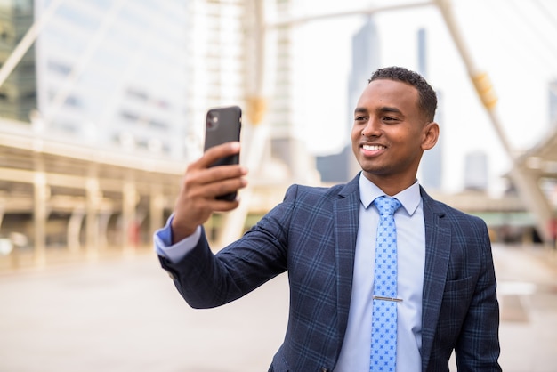 Feliz apuesto joven empresario tomando selfie en la ciudad al aire libre
