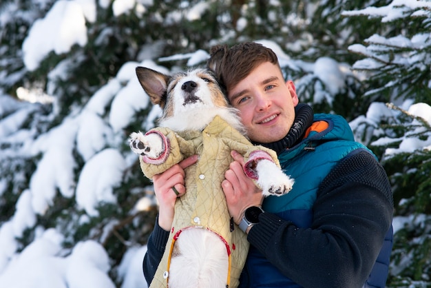 Feliz apuesto joven positivo, dueño está abrazando, sosteniendo a su perro en las manos, sonriendo, riendo