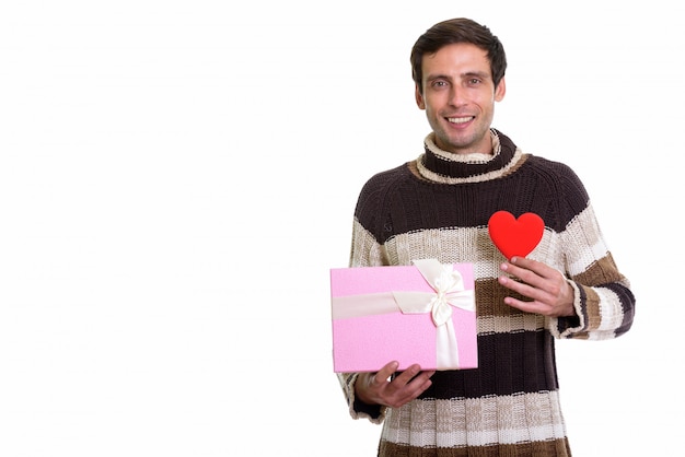 Feliz apuesto joven sonriendo mientras sostiene la caja de regalo y el corazón rojo listo para el día de San Valentín