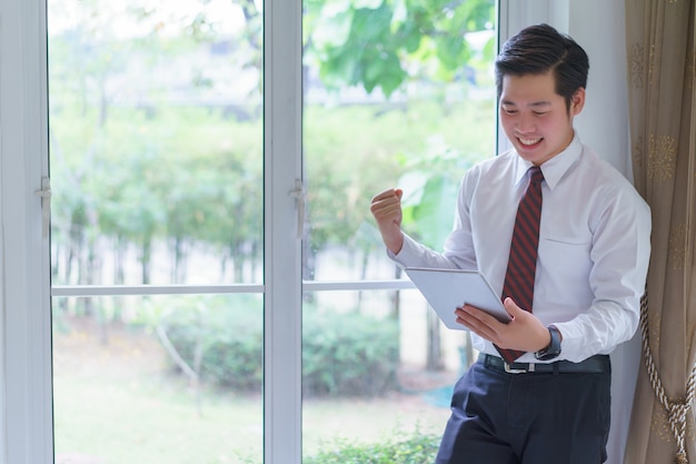 Feliz asiático jovem empresário bonito usando tablet feliz em receber lucros elevados, tem negócios prósperos.