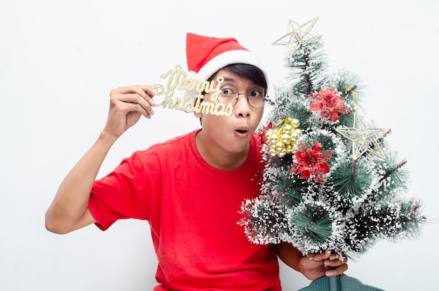 feliz y atractivo hombre asiático vestido con ropa navideña roja mientras sostiene un árbol de Navidad