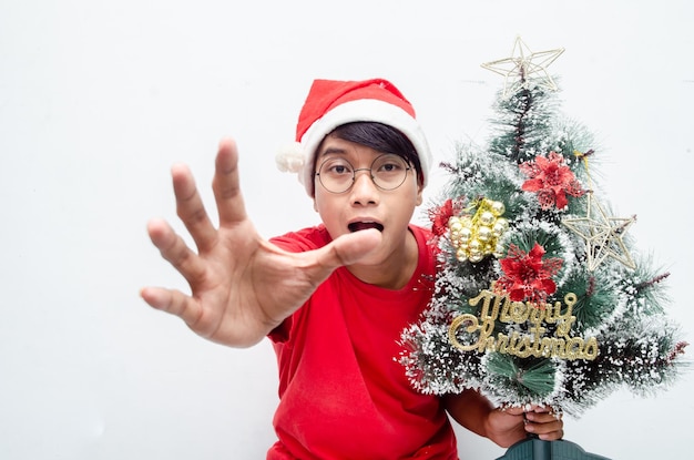 feliz y atractivo hombre asiático vestido con ropa navideña roja mientras sostiene un árbol de Navidad.