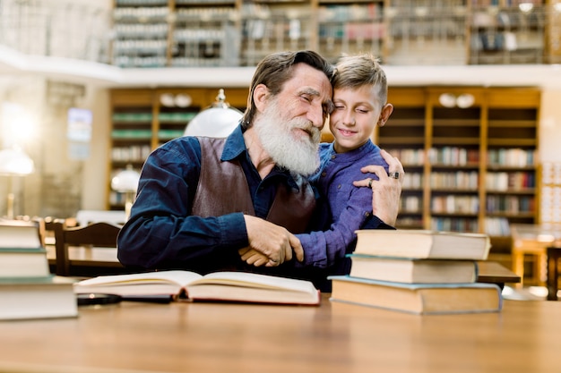 Feliz avô e neto, abraçando uns aos outros enquanto passam algum tempo juntos na biblioteca antiga vintage, lendo livros