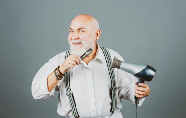 Feliz barbeiro de cabeleireiro sênior com secador de cabelo e pente secando barba e bigode retrato de idade