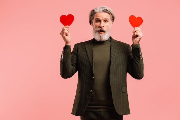 Feliz barbudo y bigote hombre maduro en traje de color caqui con corazones rojos saludo Valentine fondo rosa isoleted.