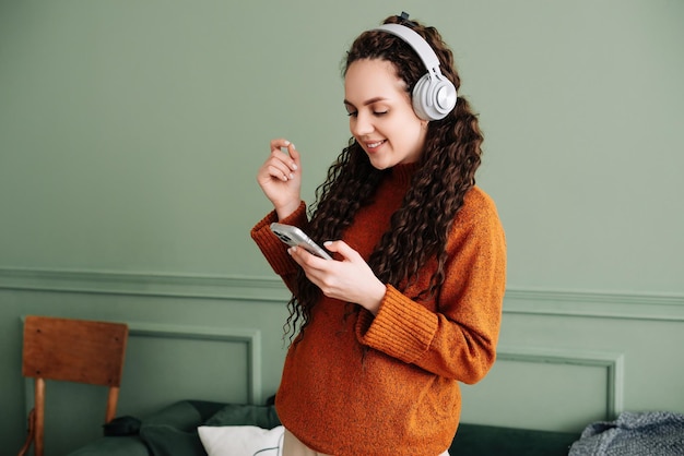 Foto feliz bastante joven con auriculares bailando en casa chica alegre escuchando música en