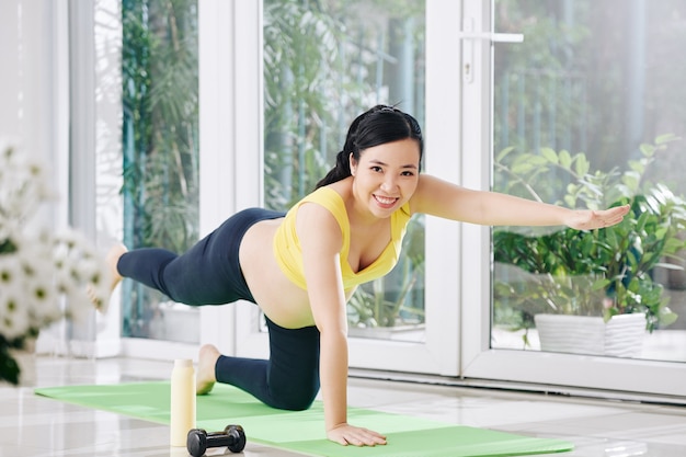 Feliz bastante joven mujer embarazada vietnamita haciendo ejercicio de equilibrio en la estera de yoga