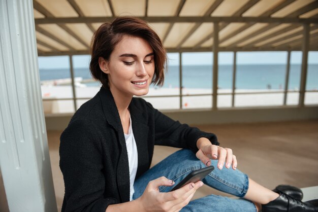 Feliz bastante joven con teléfono celular en la terraza en la playa