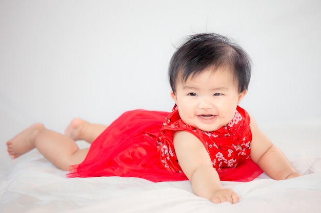 Feliz bebe asiática fofa no vestido da tradição chinesa sorrindo e rastejando na cama