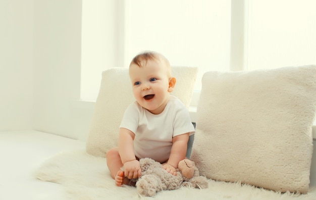 Feliz bebé lindo jugando con peluche de oso de peluche en la habitación blanca en casa