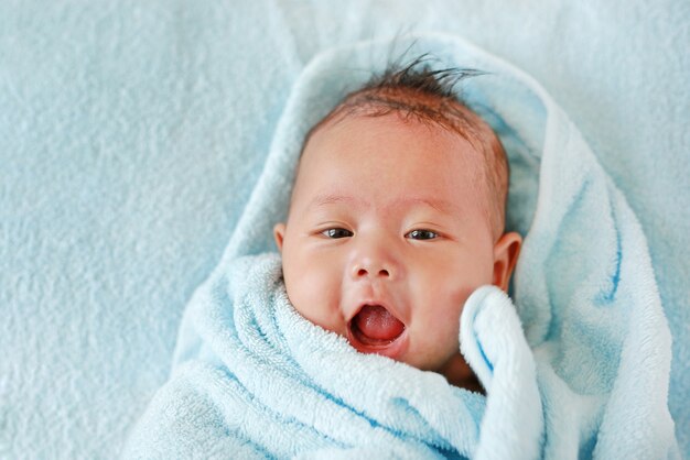 Feliz bebé niño en rollo de toalla acostado en la cama después del baño