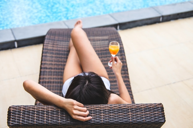 Feliz bella mujer relajante tomar el sol cerca de la piscina de lujo y la mano con naranja