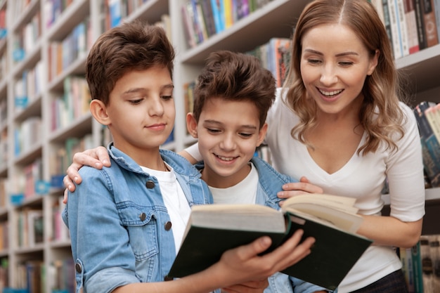 Feliz bella mujer y sus adorables hijos pequeños leyendo un libro en la biblioteca local