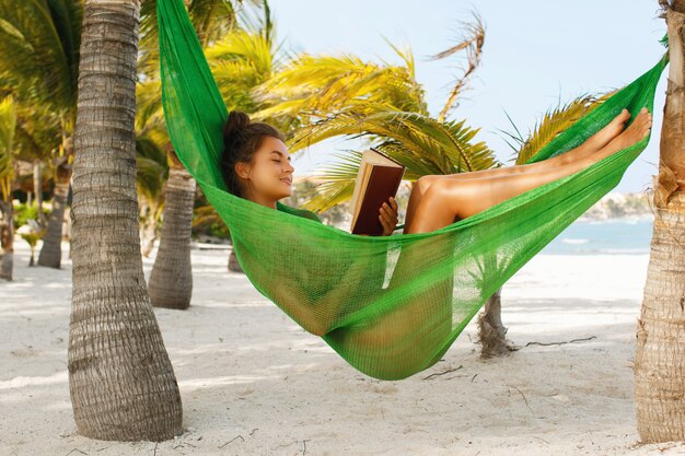 Feliz y bella mujer tumbada en la hamaca y leyendo el libro