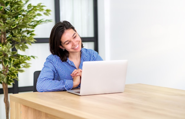 Feliz blogueira estilosa rindo enquanto conversa com amigos em redes sociais em um laptop usando internet sem fio em coworking Jovem positiva fazendo compras online no site