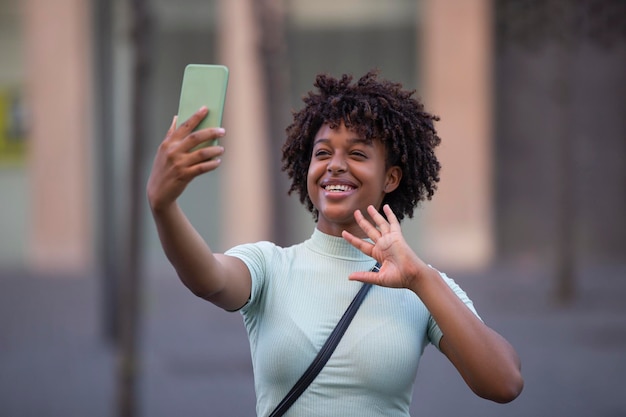 Feliz bloguera con cabello afro riéndose sosteniendo un vlog de grabación telefónica grabando una historia en las redes sociales o una videollamada en una aplicación móvil