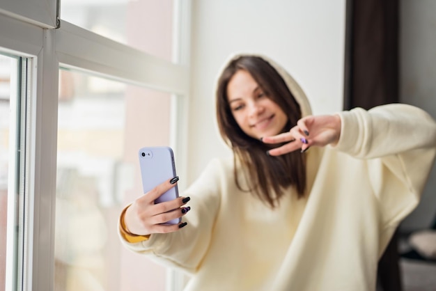 Feliz bloguera tomando un retrato selfie en la cámara de un smartphone para publicar en las redes sociales una alegre adolescente hablando en una videollamada con familiares o amigos a través de un teléfono móvil Enfoque selectivo suave